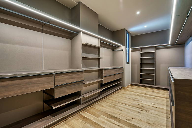 Spacious empty walk-in closet with wooden shelves, drawers, and built-in LED strip lighting.